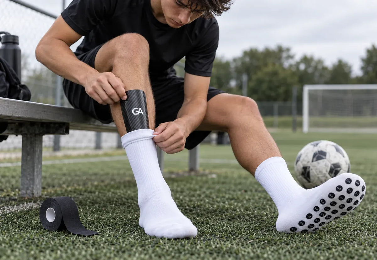 Joueur qui ajuste son mini protège-tibias sur ses grip socks blanches Grip Assist X2, au bord du terrain